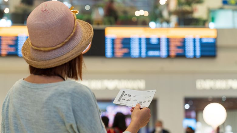 Woman holding the ticket checking the schedule from the departure board at the airport terminal